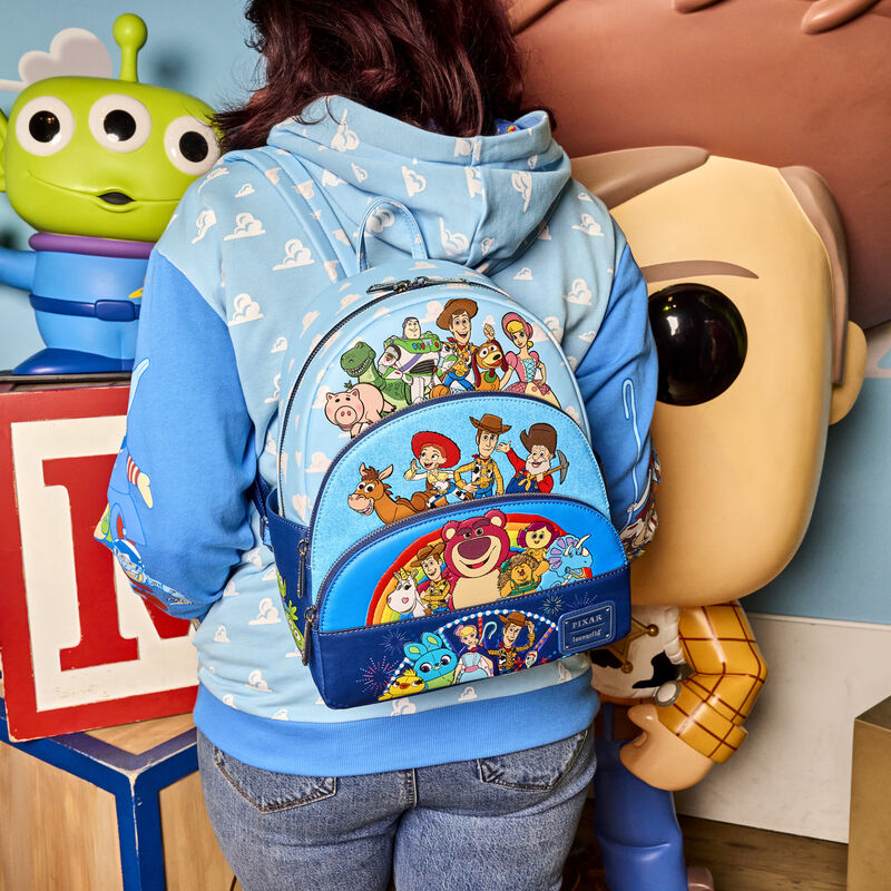 Woman facing away from camera wearing the Toy Story Movie Collab Triple Pocket Mini Backpack with large children's blocks, one the Alien's from Toy Story and a Pop! version of Woody in the background.